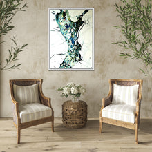 Load image into Gallery viewer, A framed abstract painting featuring a stylized tree in teal, blue, green, and black on a white background, displayed in a styled room with two wicker armchairs and a small round table.
