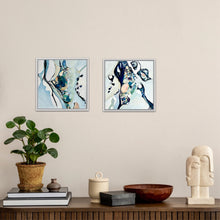 Load image into Gallery viewer, Two framed abstract art prints with blue, white, and black brushstrokes displayed side-by-side on a beige wall above a wooden console table styled with a potted plant, books, a ceramic jar, a wooden bowl, and a modern stone sculpture.

