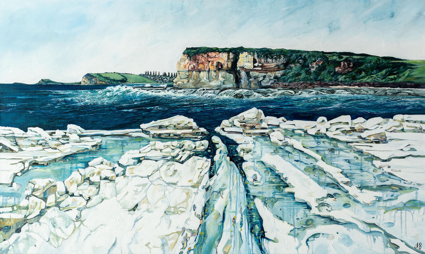 Coastal scene looking towards Werri Beach NSW, with a white rock platform, ocean swell and waves in the foreground, red cliffs in the background and a grassy headland with pine trees in the distance.