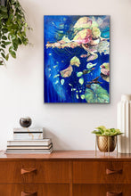 Load image into Gallery viewer, Abstract oil painting, mixed media on canvas. Royal blue with shades of green, pink and yellow. Shown in situ on a beige wall above a timber sideboard.
